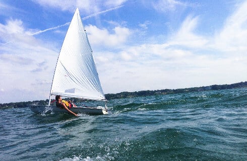 Sailboat on the blue water with waves and sun.