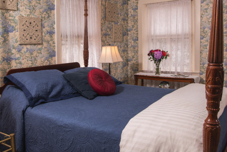 Guest room with blur lattered wallpaper and a wooden four poster bed with blue bedding