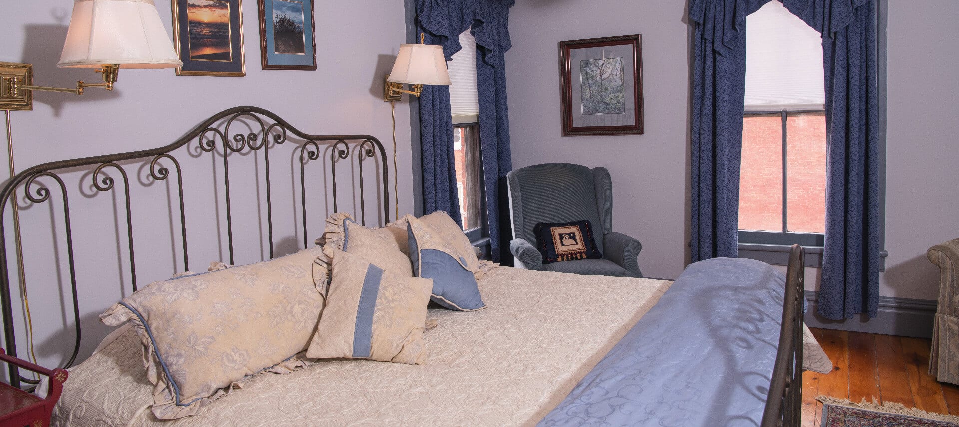 King sized bed with cream and blue bedding and a blue wingback chair.