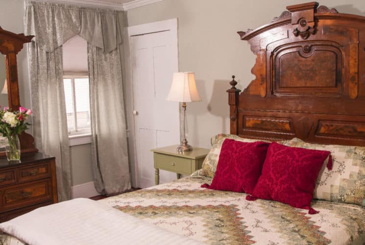 Guest room with an airy window and a large antique Eastlake bed and ceiling fan.