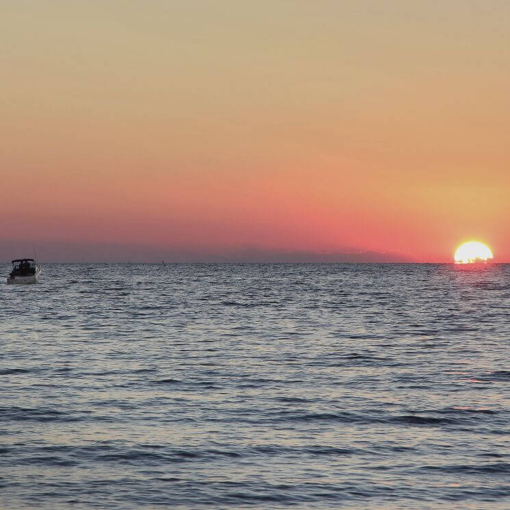 Expansive view of wide water with a boat at sunset.